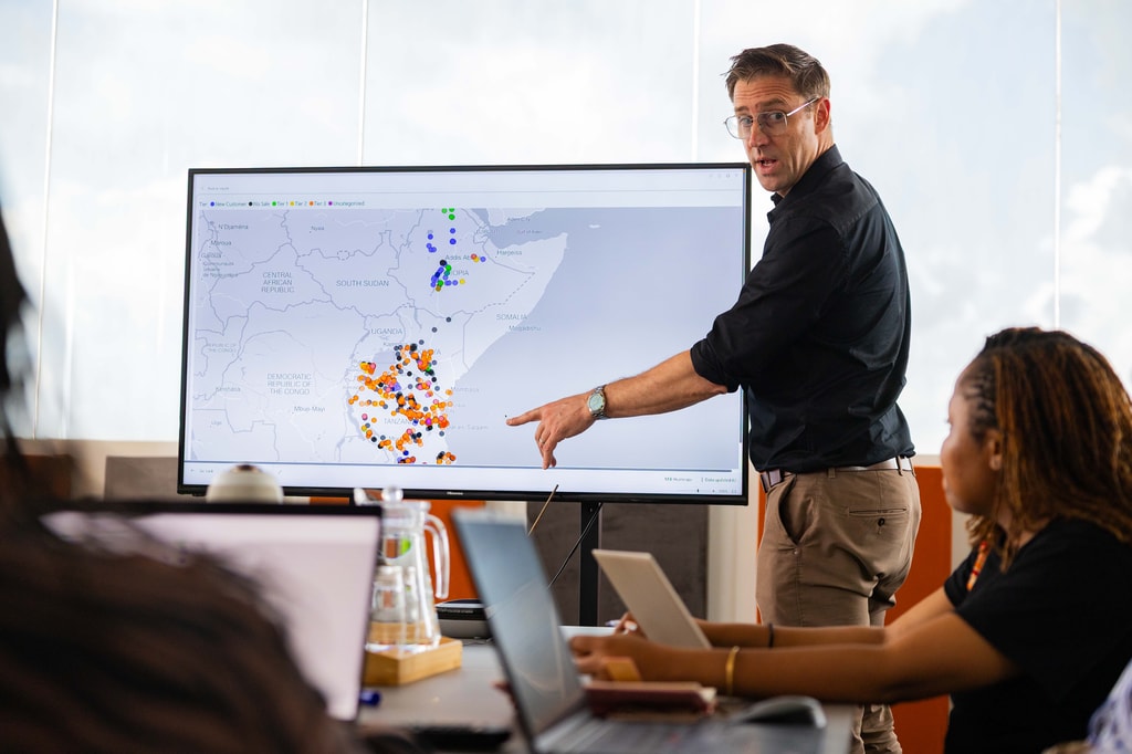 Felix Brooks-church, cofundador de Sanku, aparece dirigiendo una reunión de equipo en la oficina de Sanku en Dar es Salaam, Tanzania. En la pantalla se muestra un mapa con todos los molinos en Tanzania,
Kenia y Etiopía. Foto: © Rolex / Peter Ndung’u.