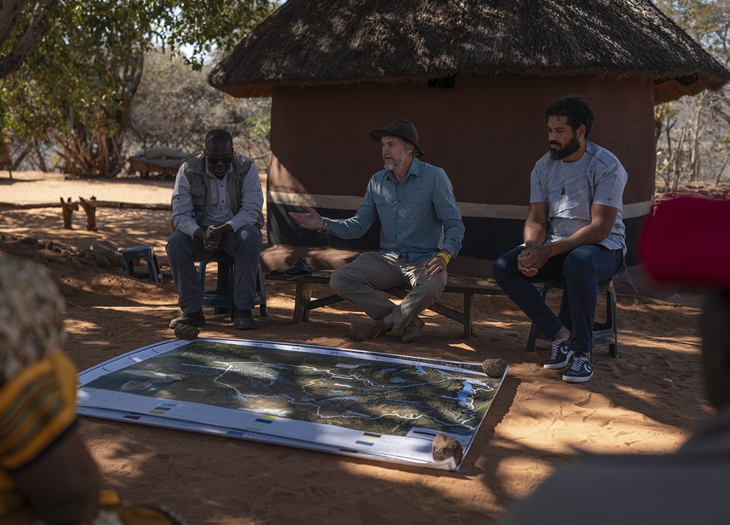 El explorador Steve Boyes (centro) y su compañero de expedición Kerllen Costa (der.) aparecen junto a reyes y jefes angoleños de comunidades situadas a lo largo de las orillas del río Zambeze mientras conversan sobre el uso del agua por parte de su pueblo. Frente a ellos se encuentra un mapa de África central. Foto: ©Rolex/Aurélie Marrier d’Unienville.