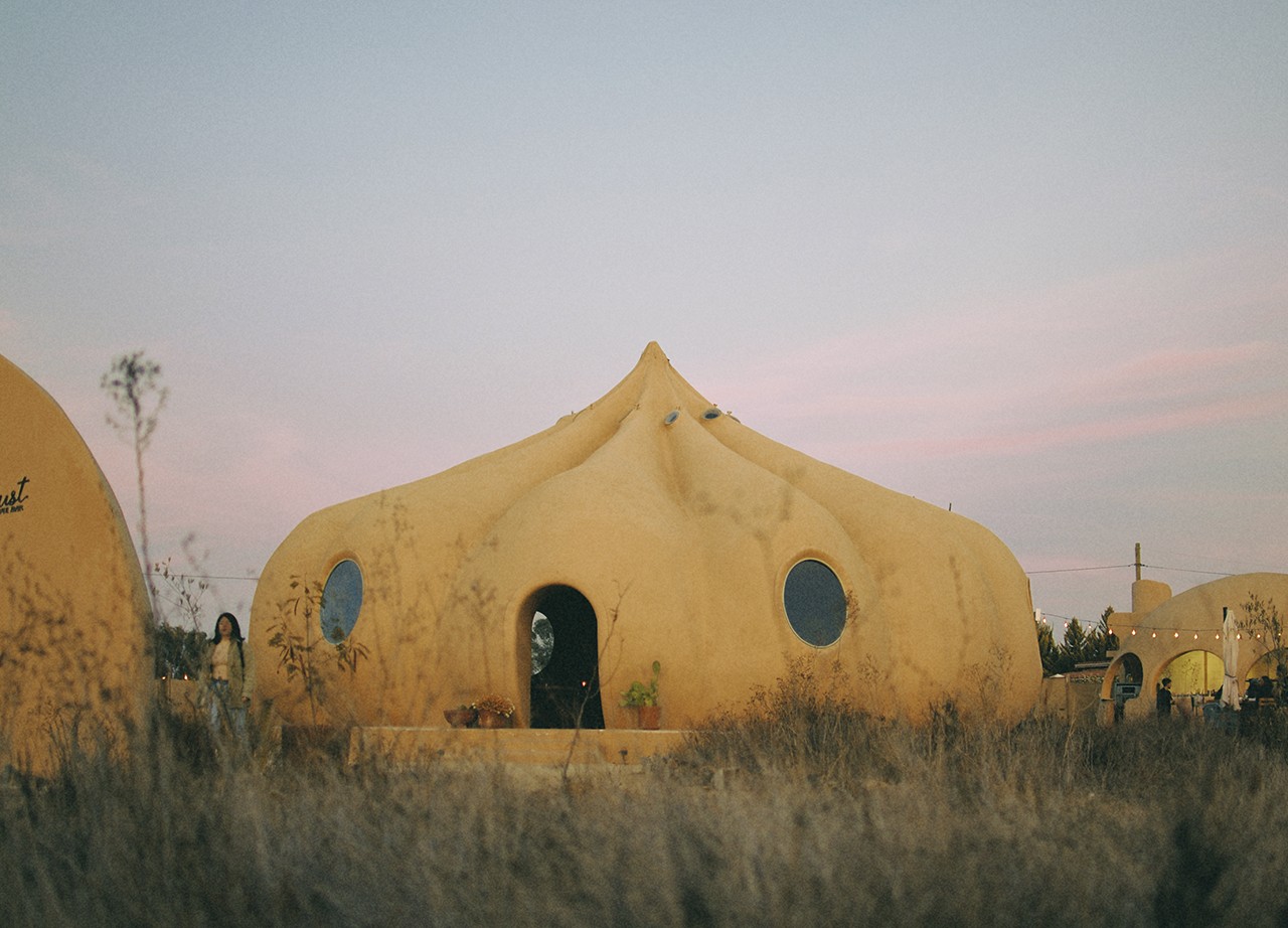 Bloodlust se aleja del bar tradicional con una arquitectura escultórica inspirada en la caída de una gota de vino, traducida en un volumen orgánico y casi surrealista dentro del paisaje del valle. Concebido a partir de la obra de Jaime Zuverza y construido con ferrocemento, el espacio articula domos y formas curvas que diluyen los límites entre interior y exterior, y lo acercan más a una instalación artística que a un wine bar convencional.